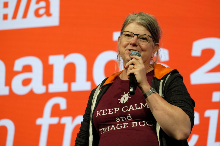 Photo of Emma Humphries speaking at an event. They are wearing a t shirt reading 'Keep Calm and Triage Bugs'